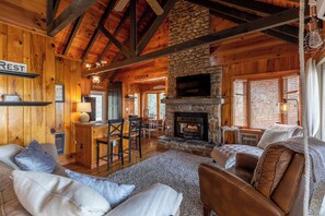 A rustic cabin interior with a stone fireplace, wooden walls, and a cozy seating area. - Heather Heights Cottage (Boone)