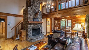 A spacious living area with a stone fireplace, leather furniture, and a wooden ceiling. - Hummingbird Hollow (Banner Elk)