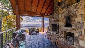 A covered outdoor seating area with stone walls and a fireplace, overlooking a scenic landscape. - Heavenly Daze at Eagles Nest (Banner Elk)
