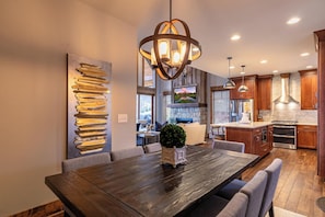 Une cuisine moderne avec des meubles en bois, une cheminée en pierre et un coin repas comprenant une grande table et des chaises en bois.