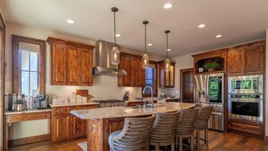 Una cocina moderna con armarios de madera, una isla grande con taburetes de bar, electrodomésticos de acero inoxidable e iluminación colgante.