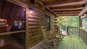 A wooden cabin with a porch, rocking chairs, and a screened-in area. - Trillium (Banner Elk)