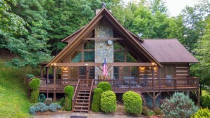 A cabin with a stone chimney, wooden deck, and a flag. - Highlander Cabin (Deep Gap)