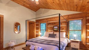 A four-poster bed with a wooden headboard, a bedside table with a lamp, and a small stool with towels. - Highlander Cabin (Deep Gap)