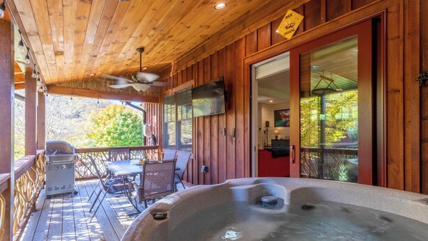 Eine Holzterrasse mit Whirlpool, Sitzgelegenheiten im Freien und einem an der Wand befestigten Fernseher.