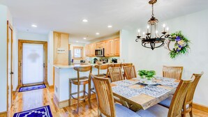 A modern kitchen with wooden cabinets, a central island, and a dining area with a chandelier and floral decoration. - Peace at Echota (Boone)