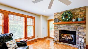 A spacious living room with a fireplace, wooden flooring, and large windows. - Peace at Echota (Boone)