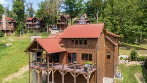 A wooden cabin with a balcony, stone foundation, and a red roof, surrounded by greenery. - Birds Nest Retreat at Eagles Nest (Banner Elk)