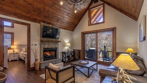 A cozy living room with a stone fireplace, wooden ceiling, and a television mounted above it. - Blue Creek Cabin at Eagles Nest (Banner Elk)