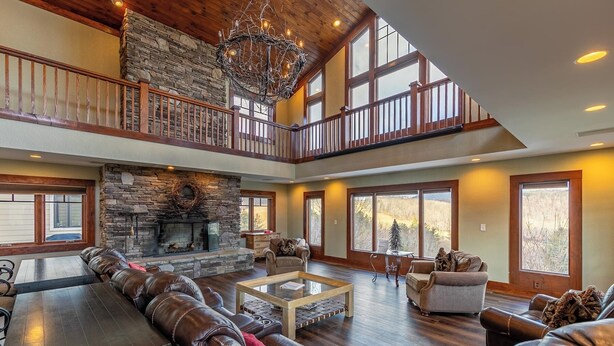 A spacious living room with a stone fireplace, leather sofas, a coffee table, and large windows offering views of the outdoors. - Sunnyside Farm (Boone)