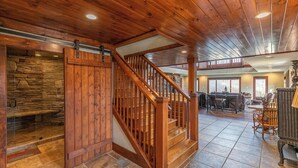 A spacious interior with a wooden staircase, stone wall, and a dining area with chairs and tables. - Sunnyside Farm (Boone)