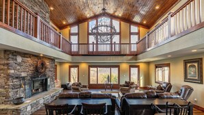 A spacious living area with a stone fireplace, leather seating, and a high ceiling with wooden beams. - Sunnyside Farm (Boone)