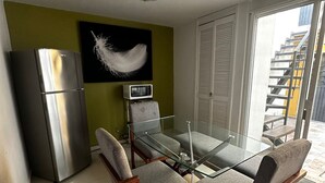 Une cuisine moderne équipée d’un réfrigérateur en acier inoxydable, d’un four à micro-ondes et d’une table à manger en verre, accompagnée de quatre chaises grises à revêtement.