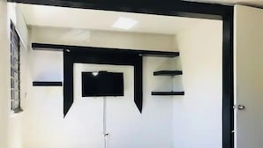 Une chambre à coucher avec un lit, un téléviseur à écran plat fixé au mur et une fenêtre avec des barreaux en métal.
