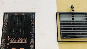Un bâtiment à deux étages, doté d’une façade blanche et jaune, d’un portail noir orné de motifs géométriques et d’une petite fenêtre avec une grille en métal noir.
