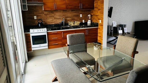 Une cuisine compacte avec des meubles de rangement en bois, une cuisinière et une table à manger en verre, accompagnée de quatre chaises.