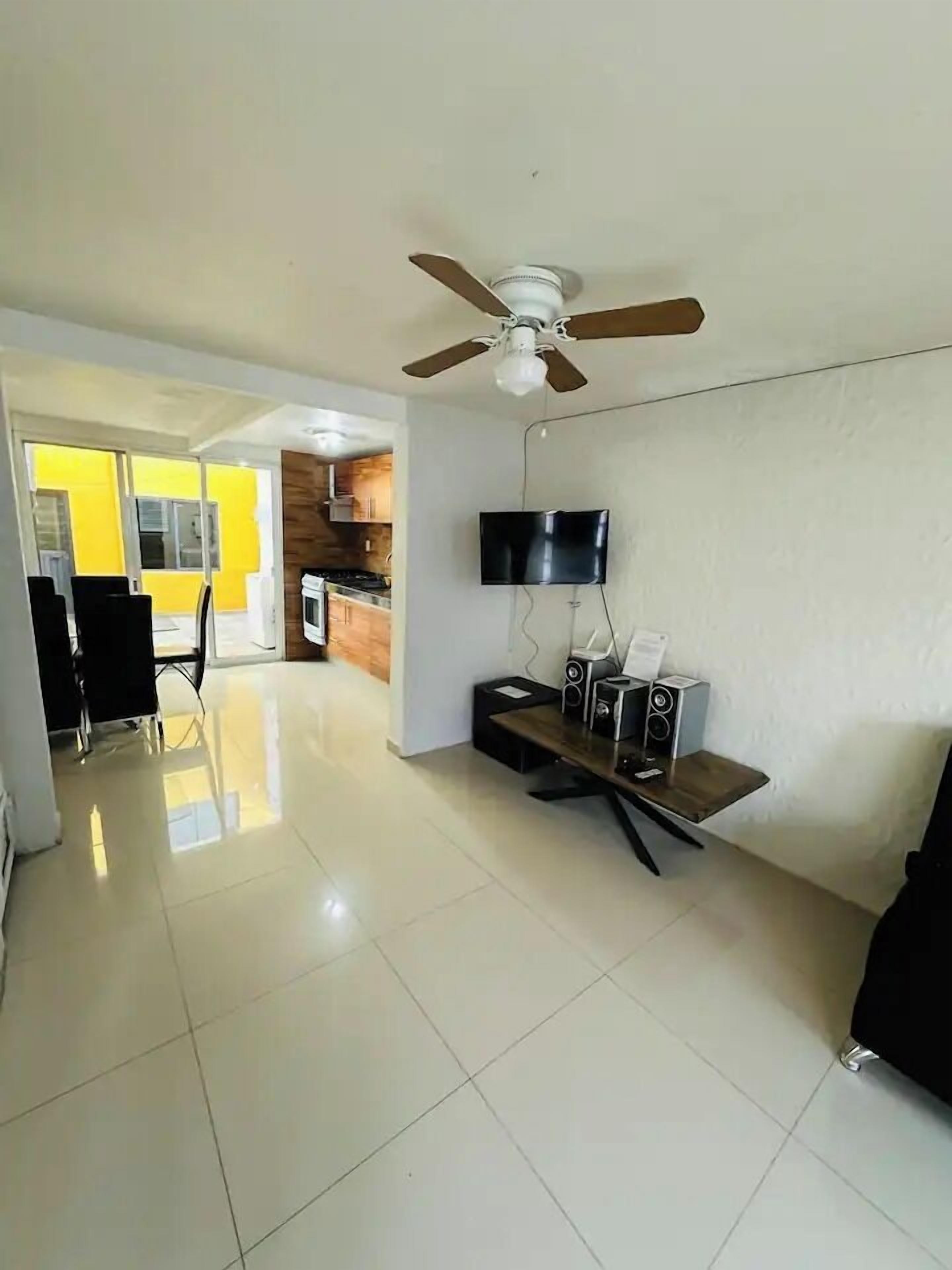 A modern living room with a ceiling fan, a flat-screen TV, and a sound system on a wooden stand.