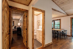 A wooden-floored hallway leading to a bathroom and a dining area with a wooden table and chairs. - Moosey Creek Lodge (Banner Elk)