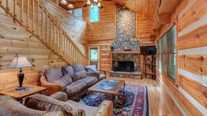 L’intérieur chaleureux d’un chalet avec une cheminée en pierre, des murs en bois, un canapé et une table basse.