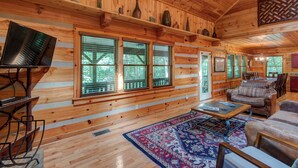 L'intérieur d'une cabane en rondins, avec un plancher en bois, de grandes fenêtres, un téléviseur, un canapé et un coin repas.