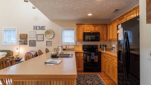 A kitchen with wooden cabinets, a black refrigerator, a microwave, and a dining area with a table and chairs. - Still Lake Haven at Echota (Boone)