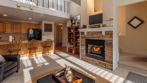 A spacious living area with a fireplace, a kitchen with wooden cabinets, a dining area with chairs, and a high ceiling with a balcony. - Still Lake Haven at Echota (Boone)