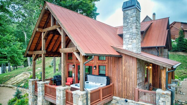 Een chalet met een stenen schoorsteen, houten terras en een bubbelbad.