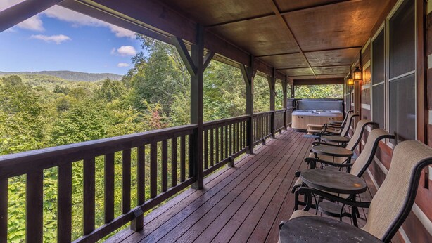 A covered porch with wooden railings, outdoor seating, and a view of a forested landscape. - Amen Corner (Vilas)