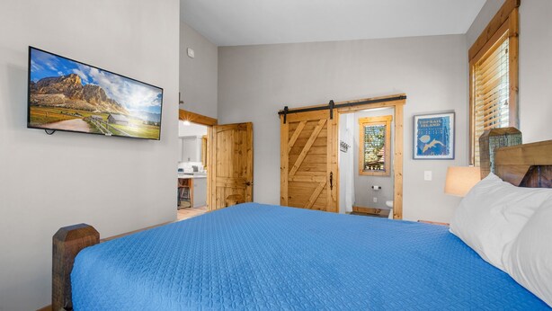 A bedroom with a large bed, wooden doors, a TV, and a poster on the wall. - Bear Woods Belle at Eagles Nest (Banner Elk)