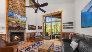 A cozy living room with a stone fireplace, a large TV mounted on the wall, and a comfortable seating area with a leather couch and armchair. - Bear Woods Belle at Eagles Nest (Banner Elk)