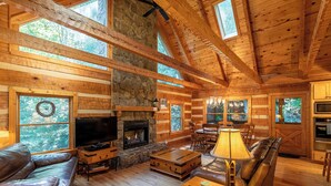 A log cabin interior with a stone fireplace, leather furniture, and large windows. - Skylark (Banner Elk)