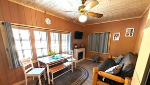 A cozy room with a wooden ceiling, a dining table with chairs, a sofa, a fireplace, and a clock on the wall. - 2BR 1BA Cabin #2 Riverside Point Resort (Park Rapids)