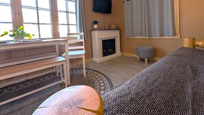 A room with a wooden floor, a fireplace, a television, a window with curtains, and a bed. - 2BR 1BA Cabin #2 Riverside Point Resort (Park Rapids)