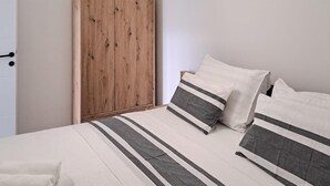 A bedroom with a wooden wardrobe, a bed with striped bedding, and a white towel on the floor. - Gorgeous apartment in Pirovac with WiFi (Pirovac)
