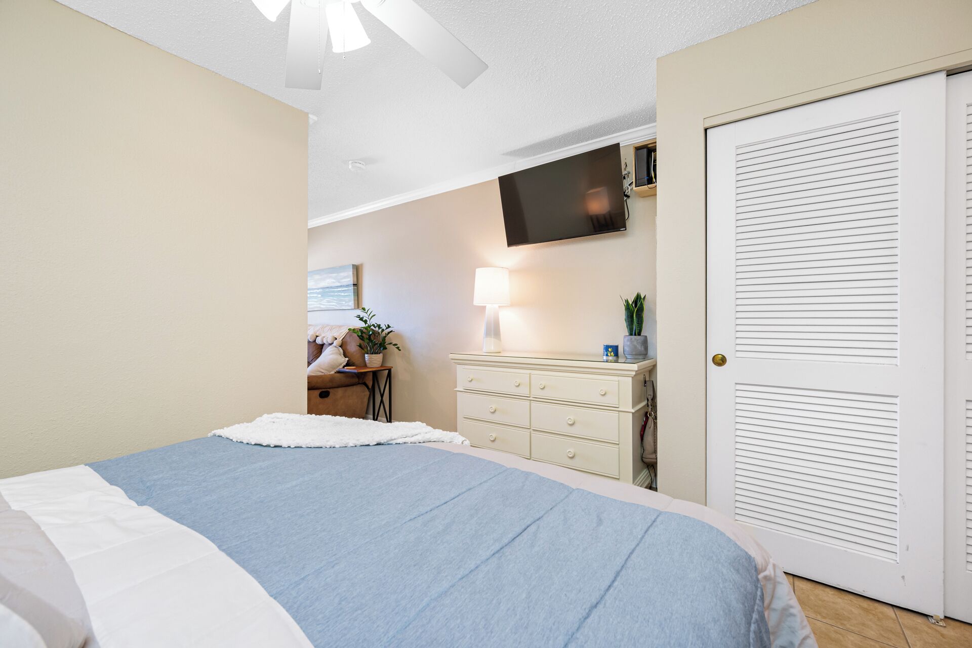 Une chambre à coucher avec un lit, une commode, un téléviseur et une porte.