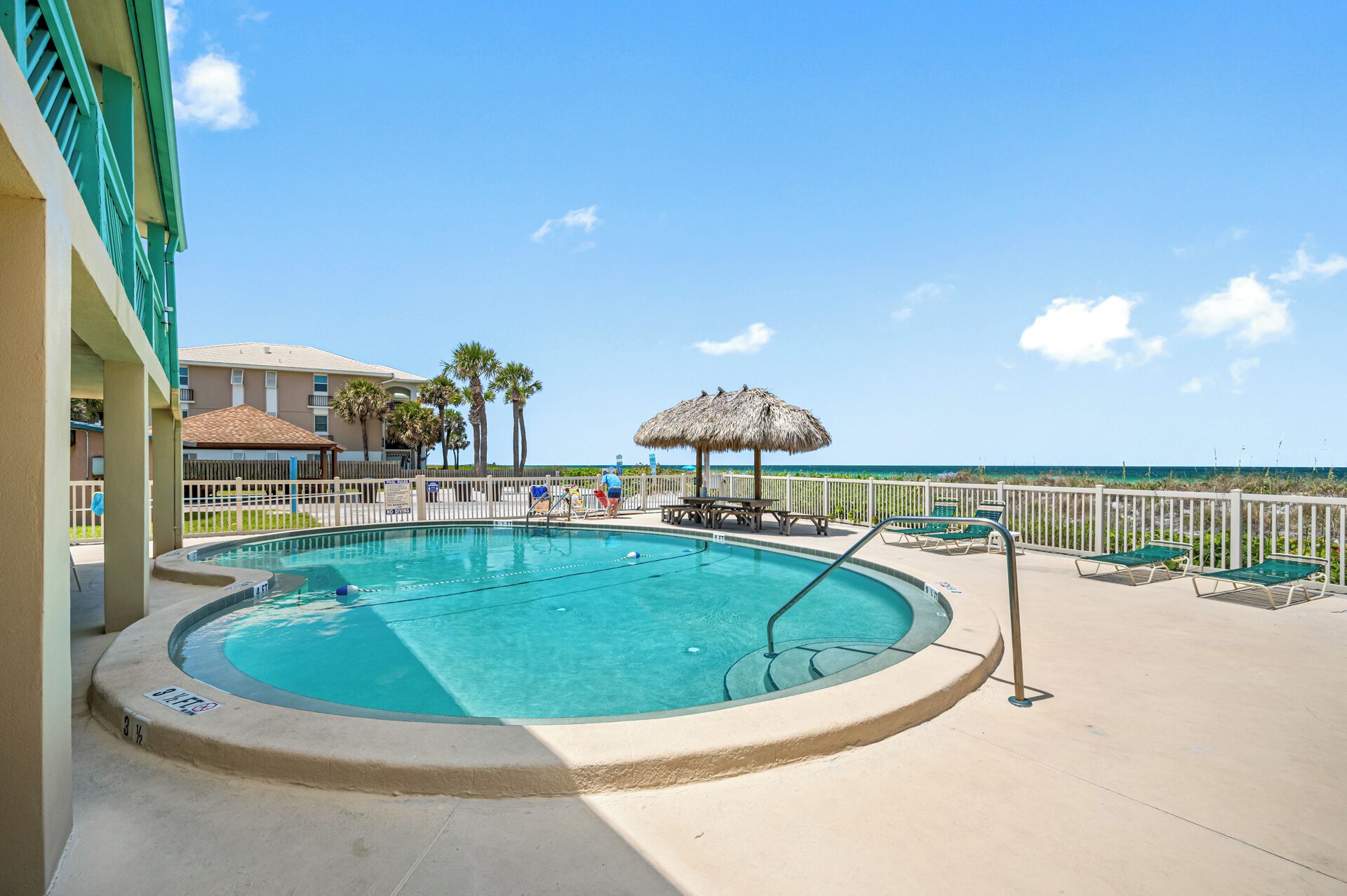 A pool area with a thatched umbrella, lounge chairs, and a view of the ocean.