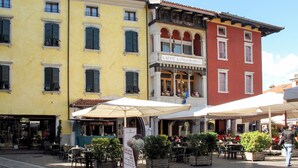 A street with outdoor seating at cafes, a building with a sign 'CAFFE' LONGOBARDO', and a shop with 'PASTICCERIA' and 'GLAS' signs.