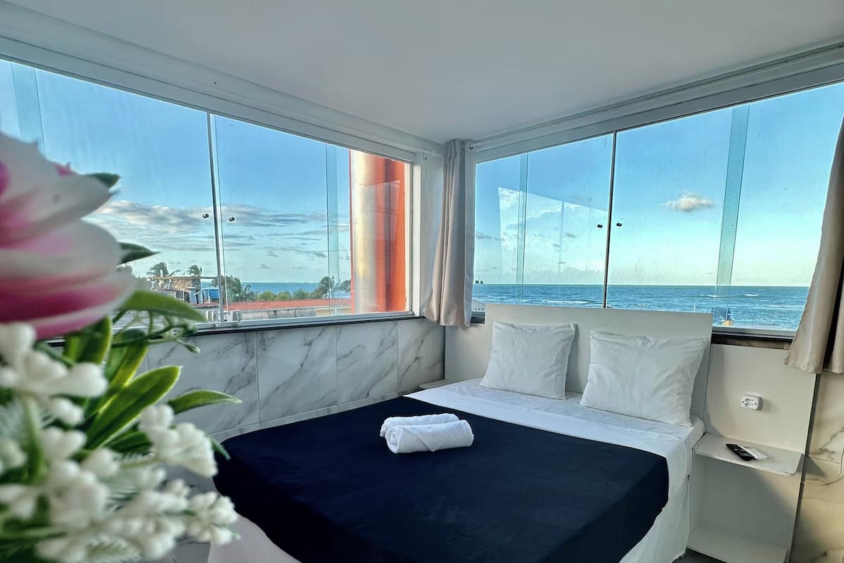 A bedroom with a large bed, white bedding, and a view of the ocean.