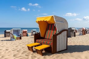 Una silla de playa con dosel amarillo y cojines a rayas, un banco de madera y cabañas de playa al fondo.