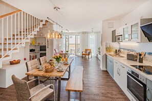 A modern kitchen with wooden flooring, a dining area with a wooden table, and a staircase with white railings.