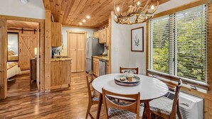A wooden interior with a dining table, chairs, a chandelier, and a view of greenery through the window. - Lovely Condo in Downtown Blowing Rock (Blowing Rock)