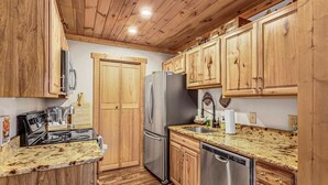 A compact kitchen with wooden cabinets, a stainless steel refrigerator, a dishwasher, and a granite countertop. - Lovely Condo in Downtown Blowing Rock (Blowing Rock)
