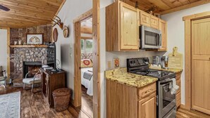 A cozy cabin-style kitchen with a stone fireplace, wooden cabinets, and a stone wall. - Lovely Condo in Downtown Blowing Rock (Blowing Rock)