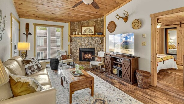 A cozy living room with a stone fireplace, a ceiling fan, and a television. - Lovely Condo in Downtown Blowing Rock (Blowing Rock)