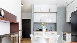 Una cucina moderna con mobili bianchi, un frigorifero nero e un'area pranzo con sedie bianche e un tavolo di legno.