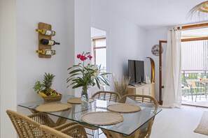 A modern dining area with a glass table, wicker chairs, a vase with flowers, and a fruit basket. - Cofisa Great Blue (Javea / Xàbia)
