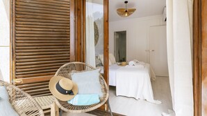 Quarto com cama, uma cadeira e janela com persianas de madeira.