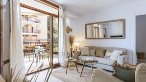 Sala de estar com sofá, mesa de centro de vidro e área de jantar visível através de uma porta de correr de vidro.