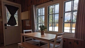 A wooden interior with a dining table, chairs, a bench, a potted plant, and a door with curtains.