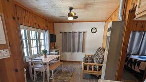 A cabin interior with a dining area, a sofa, a stove, and a ceiling fan.